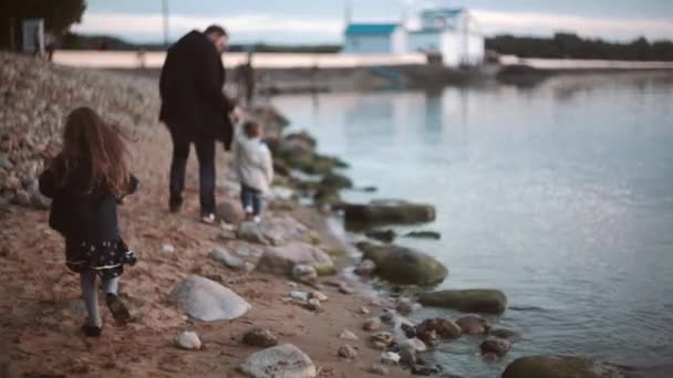 Bakifrån av far och son promenader längs stranden, dotter går till dem. Bror och syster umgås med pappa — Stockvideo