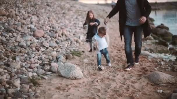 Vista frontal de padre e hijo caminando a lo largo de la orilla, hija corre hacia ellos. Hermano y hermana pasando tiempo con papá . — Vídeos de Stock