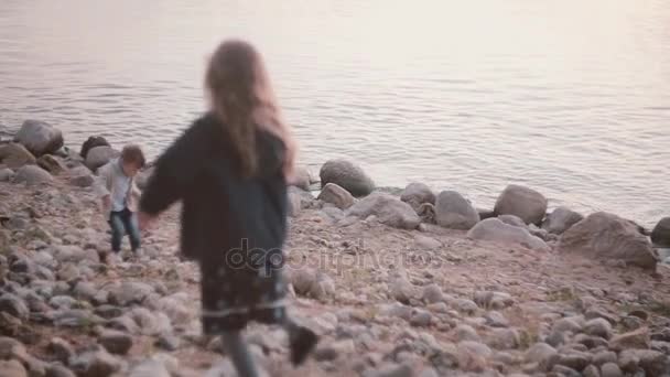 Broer en zus samen spelen op de oever. Jongen en meisje lopen door de stenen in de buurt van het water. — Stockvideo