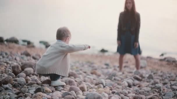 Little boy making steps on the rocks. Mother waiting son in the distance and supports boy. Male falls but rises and try. — Stock Video