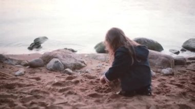 Kıyıda oturan ve kumla oynayan sevimli küçük kız. El kum ve yere dökülen o alır.