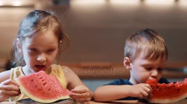 Kız ve erkek kardeşim mutfak masada oturuyor. Erkek ve kız plaka üzerinde sulu karpuz yeme ısırıkları parçaları.
