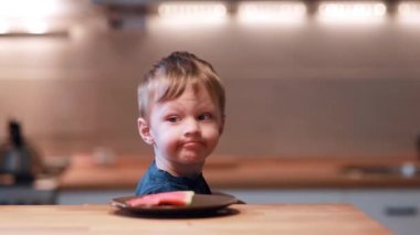 Masada oturan küçük çocuk kafa döner ve bir tabağa karpuz görür. Erkek sevinç not ve bir ısırık al.