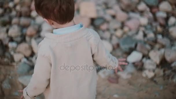 Aranyos kisfiú futó áttérés egyik lábát a másik közelében a kövek, homok. Férfi séta kívül. — Stock videók