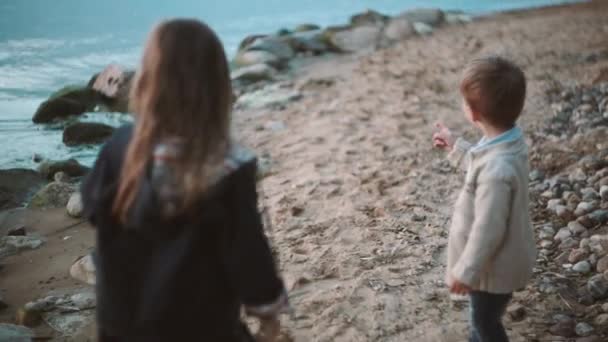 弟弟和妹妹一起度过时间靠近水的地方。小男孩和女孩走在海岸上. — 图库视频影像