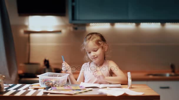 Niña sentada a la mesa y dibujando con bolígrafo de colores en habitación grande con luz suave. Tocando la nariz . — Vídeos de Stock