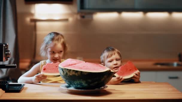 Hermano y hermana sentados a la mesa en la cocina. Niño y niña comiendo sandía, disfrutando de la fruta . — Vídeos de Stock