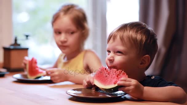 Duas crianças bonitos menina e menino comendo uma melancia. Irmão e irmã sentados à mesa, comam juntos. . — Vídeo de Stock