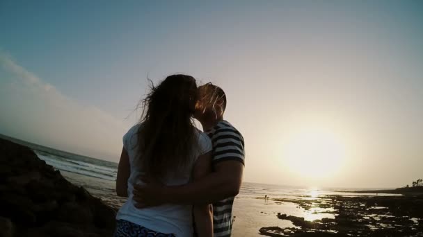 Man och kvinna stående på stranden vid havet, kramas och kyssas på solnedgången. Par på sunset beach. — Stockvideo