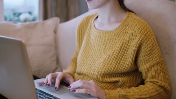 Mujer joven sentada en el sofá y trabajando en el ordenador portátil, utilizando la computadora, navegar por Internet . — Vídeos de Stock
