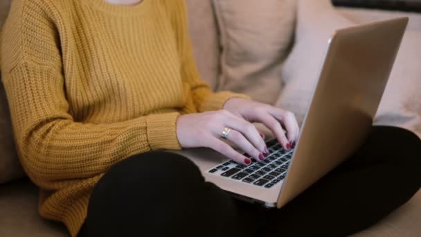 Närbild av kvinnliga händer arbetar på laptop sitter i soffan hemma. — Stockvideo