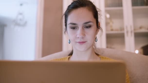 Mujer joven sentada en el sofá en la sala de estar y el uso de ordenador portátil. Navegación femenina por Internet . — Vídeo de stock