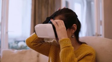 Koltukta oturan Vr-kulaklık sanal gerçeklik evde, gözlüklü genç kadın.