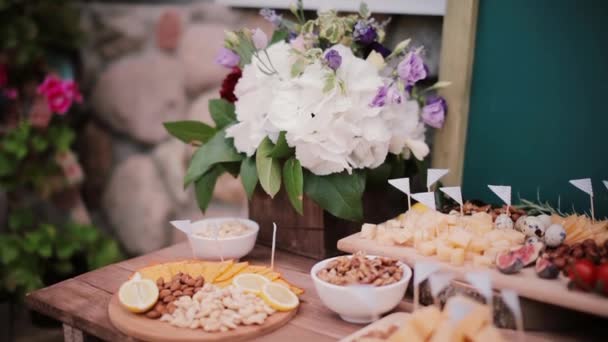 Table à fromage avec d'autres collations. Fleurs, tranches de fromage, noix, œufs et tomates sur une planche de bois . — Video