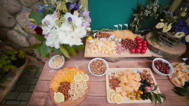 Table à fromage avec autres collations à l'extérieur. Fleurs, tranches de fromage, noix, œufs, boissons et tomates. Vue du dessus . — Video