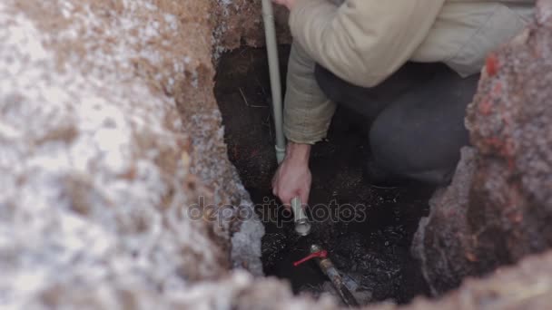 Homem de pé em um buraco na terra e fazendo reparação do sistema de água. Encanador instalando um tubo de plástico cinza . — Vídeo de Stock