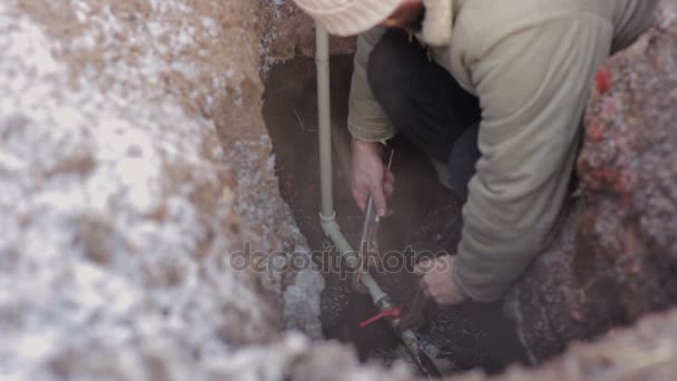 Человек в яме в земле и делает аварийный ремонт системы водоснабжения. Сантехник, работающий с серой пластиковой трубой . — стоковое видео
