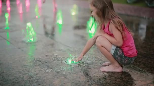 Menina brincando com jatos de água coloridos na fonte. Criança tocando fluxo com a mão, fica em um jato de água . — Vídeo de Stock