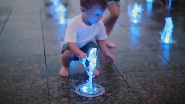 Menino bonito brincando com jatos de água coloridos na fonte no dia quente de verão, correndo para o grupo de crianças — Vídeo de Stock