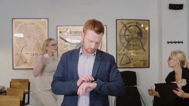 Hombre joven caminando por la oficina y utilizando la aplicación de reloj inteligente. El hombre de negocios toca la pantalla y sonríe. Movimiento lento . — Vídeos de Stock