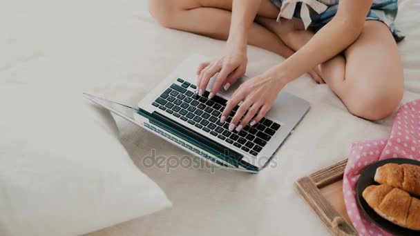 Junge Frau mit drahtloser Technologie sitzt auf einem weißen Bett zu Hause. Nahaufnahme von Mädchen, die am Laptop chatten — Stockvideo