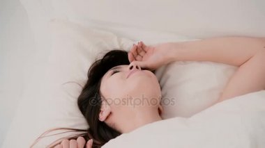 Genç kadın uyanır ve yatakta iyi eğlenceler. Çarşafın altına saklanıyor, komik surat ve saç üfleme için kız Başlat
