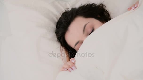 Nahaufnahme einer jungen schönen Frau mit lustigem Blick, die sich unter der Decke versteckt. Mädchen mit Spaß im Bett. — Stockvideo