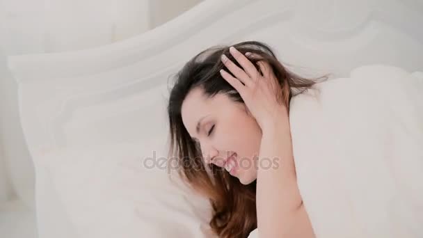 Jonge brunette vrouw liggend op het bed en het spelen met haar in lichte appartement. Meisje kijkt naar de camera en schattige glimlach. — Stockvideo