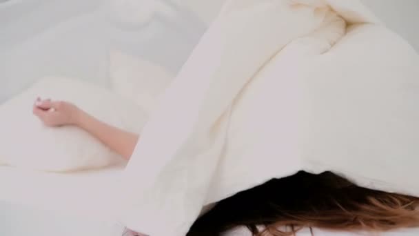 Menina bonita deitada na cama e sorrindo. Jovem mulher se esconde sob a folha, flertando com a câmera . — Vídeo de Stock