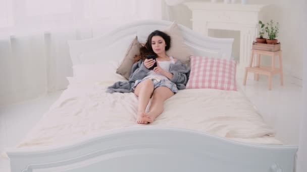 使用无线技术，躺在床上和在触摸屏上打字的年轻女人。女孩在早上浏览互联网. — 图库视频影像