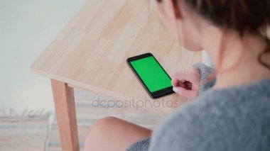 Masada oturan ve mutfakta kahve içme kadın arkadan görünüm. Esmer kız smartphone, yeşil ekran kullanır.