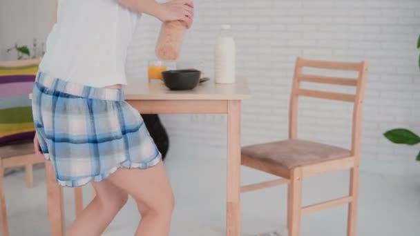 Joyeux jeune femme en pyjama préparant des flocons pour le petit déjeuner et dansant dans la cuisine légère. S'amuser le matin . — Video