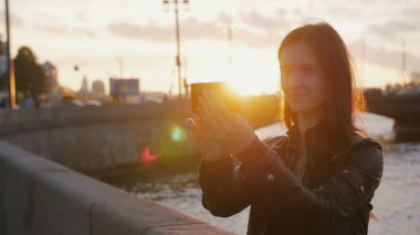 Batan güneşin parlak ışınları Bridge'de arka plan üzerinde selfie alarak genç güzel kız. 4k