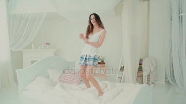 Mutlu genç kadın yatağında dans Pijama giyiyor. Esmer kız sabah mutlu hissediyor. Ağır çekim.