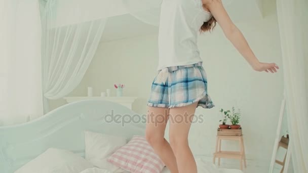 Ευτυχισμένη κοπέλα φορώντας πιτζάμες άλμα στο κρεβάτι της. Ελκυστική κοπέλα αίσθηση χαρούμενος, χέρια τεντωμένα. Αργή κίνηση. — Αρχείο Βίντεο