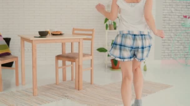 Αστεία νεαρή γυναίκα που χορεύει στην κουζίνα, τρέχει μέσα από το δωμάτιο φορώντας πιτζάμες το πρωί. Αργή κίνηση. — Αρχείο Βίντεο