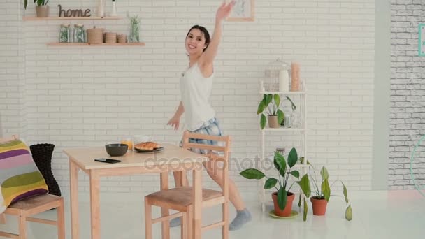 Ευτυχισμένη γυναίκα που χορεύει στην κουζίνα φορώντας πιτζάμες πρωί. Μελαχρινή κοπέλα σε εύθυμη διάθεση εχόντων διασκέδαση μόνοι. Αργή κίνηση. — Αρχείο Βίντεο