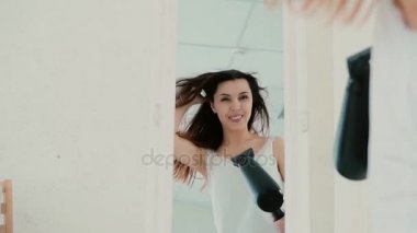 Pijama ayna önünde duran genç kadın. Saç kurutma makinesi kullanan kız ve şarkı, Rüzgar saç üfleme. Ağır çekim.