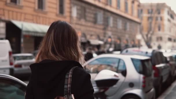 Rückansicht einer jungen Frau, die in der Innenstadt spazieren geht und sich umsieht. Brünettes Mädchen mit Rucksack erkundet neuen Ort. — Stockvideo