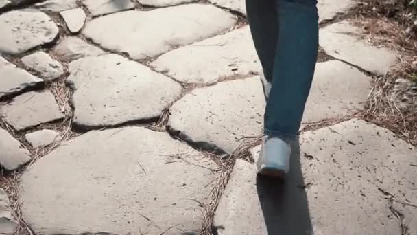 Una mujer caminando por el camino empedrado de adoquines, a la antigua. Chica explorando nueva ciudad vistiendo zapatillas. Vista de primer plano . — Vídeo de stock