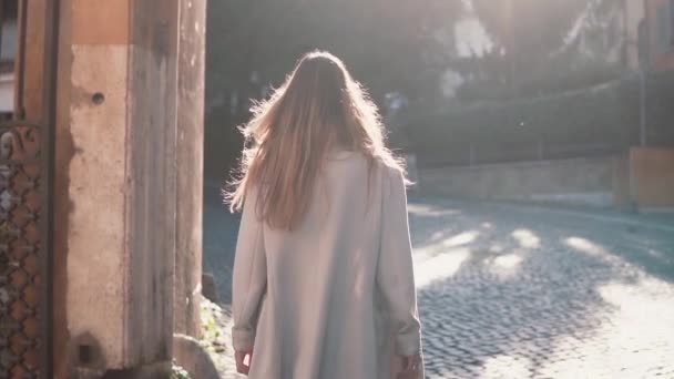 Achteraanzicht van vrouw lopen op zonnige lente stad straat in Europa. Stijlvolle meisje verkennen van de oude stad alleen. — Stockvideo