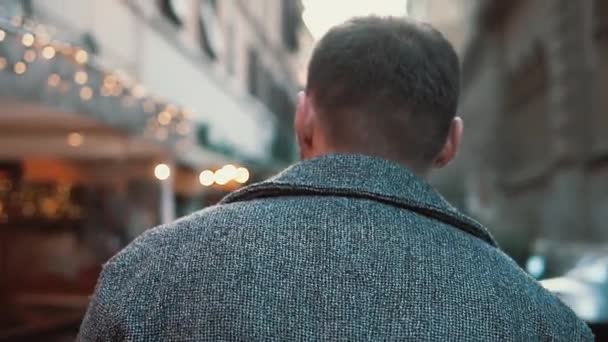 Вид сзади на молодого человека, идущего по городской улице в Европе. Стильный парень путешествует по старому городу в одиночестве, осматривается вокруг . — стоковое видео