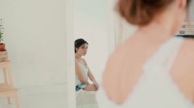 Aynanın önünde oturan ve bir yansıması arıyorum ciddi kız. Kadın kendini analiz bir pijama. Ağır çekim.