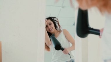 Yatak odasında şarkı, yansıma aynaya bakarak mutlu genç kadın. Kız saç kurutma makinesi ve dansları kullanır. Ağır çekim.