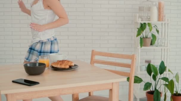 Jovem salta com alegria na cozinha depois de ouvir uma boa notícia. Menina feliz na dança durante o café da manhã. Movimento lento . — Vídeo de Stock