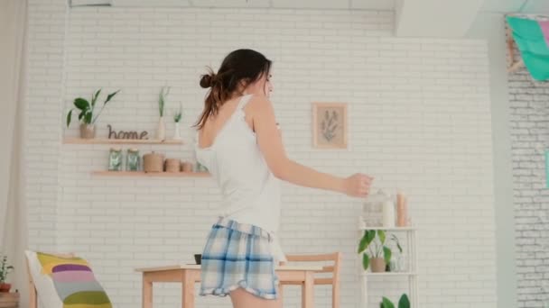 Όμορφη νεαρή γυναίκα στην κουζίνα χορό το πρωί. Μελαχρινή κοπέλα φορώντας πιτζάμες εχόντων διασκέδαση στο σπίτι. Αργή κίνηση. — Αρχείο Βίντεο