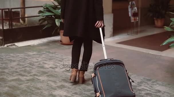 Vista trasera de las piernas de mujer viajera caminando con una maleta en la calle. Chica sale de la entrada en la ciudad . — Vídeos de Stock