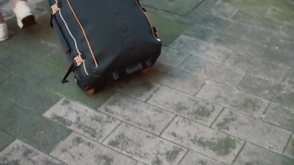 Rückansicht der Beine einer Reisenden, die mit einem Koffer auf der Straße läuft. Mädchen mit Rucksack geht aus dem Eingang. — Stockvideo