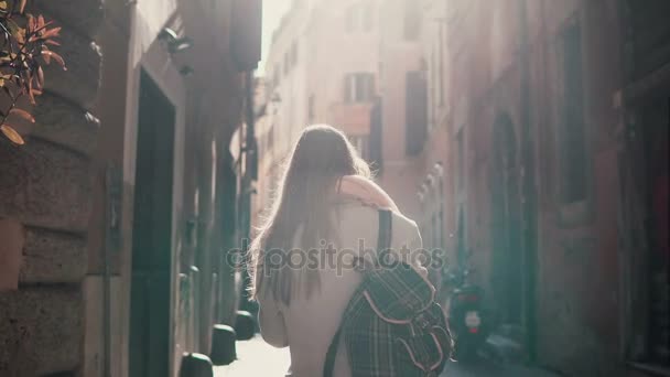 Vista trasera de la joven mujer caminando por la calle de la ciudad en Europa por la mañana. Chica explorando el casco antiguo solo, mirando a su alrededor . — Vídeos de Stock