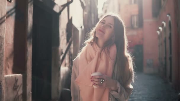 Retrato de uma jovem mulher sorrindo olhando para a câmera. Menina morena feliz de pé na rua da manhã e beber café . — Vídeo de Stock